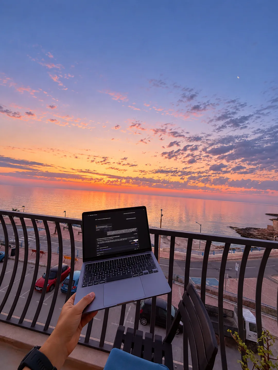 Laptop held up on a seaside balcony at sunset